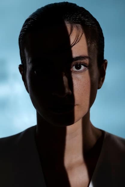 A close-up shot of a character's face in the shadows, with a subtle expression indicating inner conflict and deception.